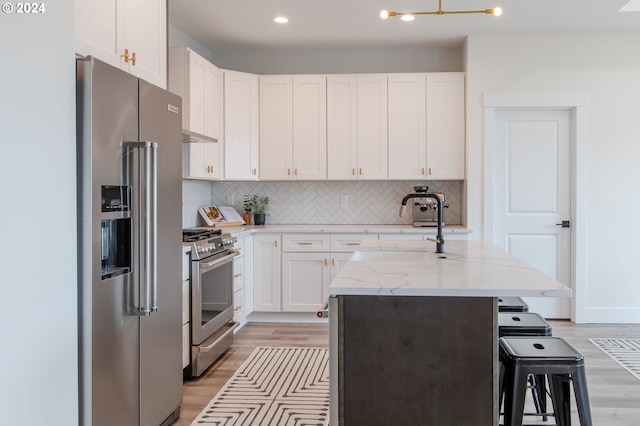 kitchen featuring white cabinetry, light hardwood / wood-style floors, appliances with stainless steel finishes, and a kitchen island with sink