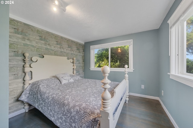 bedroom with a textured ceiling, dark wood-type flooring, and wood walls