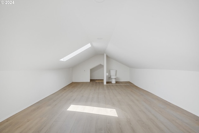 additional living space with lofted ceiling with skylight and light hardwood / wood-style flooring