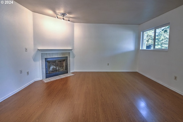 unfurnished living room featuring wood-type flooring and a tiled fireplace