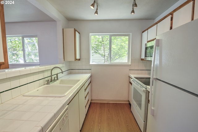 kitchen featuring sink, light wood-type flooring, white cabinets, decorative backsplash, and white appliances