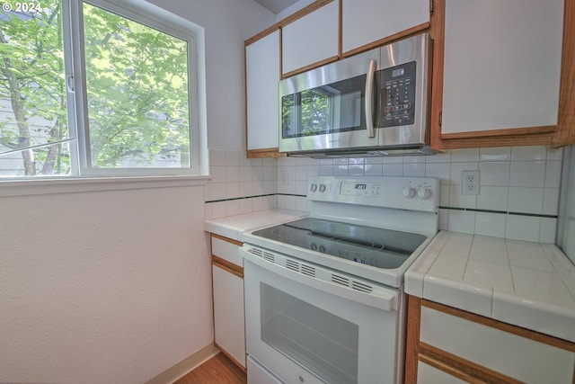 kitchen featuring backsplash, tile countertops, white cabinets, and white range with electric stovetop