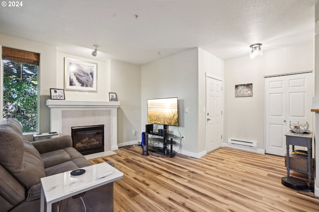 living room featuring baseboard heating, a tiled fireplace, light hardwood / wood-style flooring, and a textured ceiling