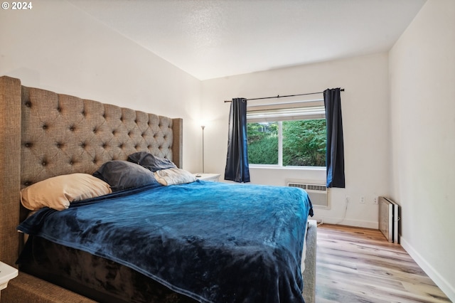 bedroom featuring a wall unit AC, radiator heating unit, and light hardwood / wood-style flooring