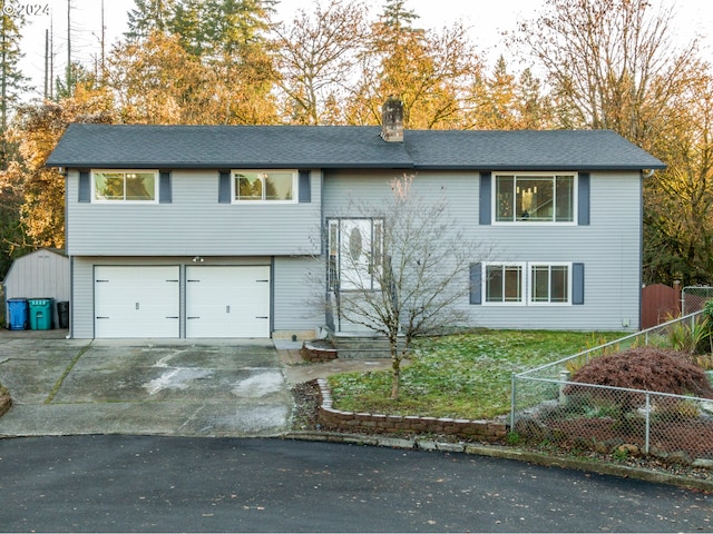 raised ranch featuring an attached garage, a chimney, fence, and concrete driveway