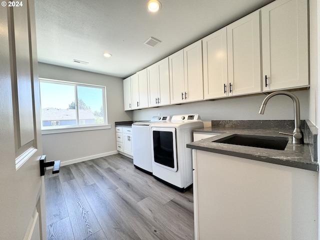 laundry room featuring sink, cabinets, washer and dryer, and light hardwood / wood-style floors