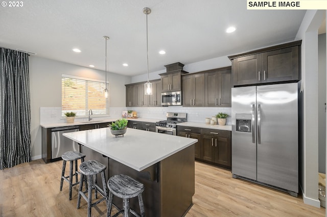 kitchen with sink, appliances with stainless steel finishes, decorative light fixtures, and light wood-type flooring