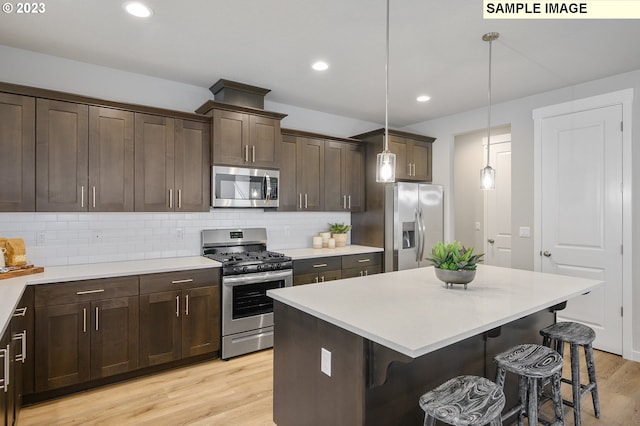 kitchen with light hardwood / wood-style flooring, hanging light fixtures, a breakfast bar, appliances with stainless steel finishes, and tasteful backsplash