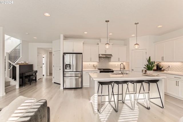 kitchen with sink, appliances with stainless steel finishes, white cabinetry, hanging light fixtures, and a center island with sink