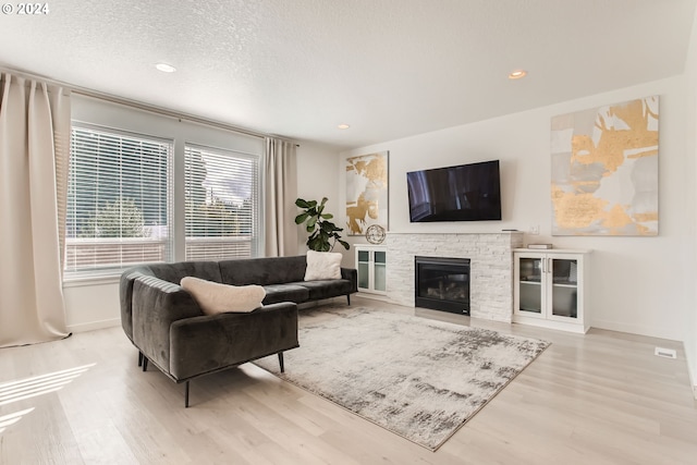 living room featuring a stone fireplace, a textured ceiling, and light wood-type flooring