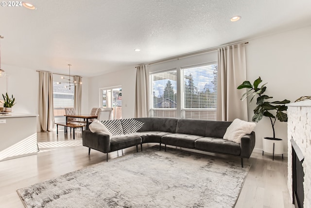 living room featuring a notable chandelier, a fireplace, a textured ceiling, and light wood-type flooring