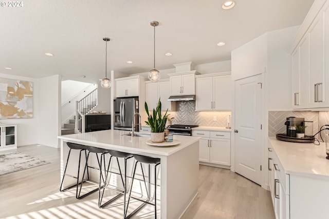 kitchen with stainless steel appliances, white cabinetry, hanging light fixtures, and a center island with sink