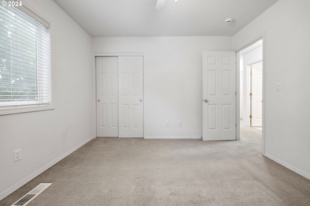 unfurnished bedroom with light colored carpet, ceiling fan, and a closet