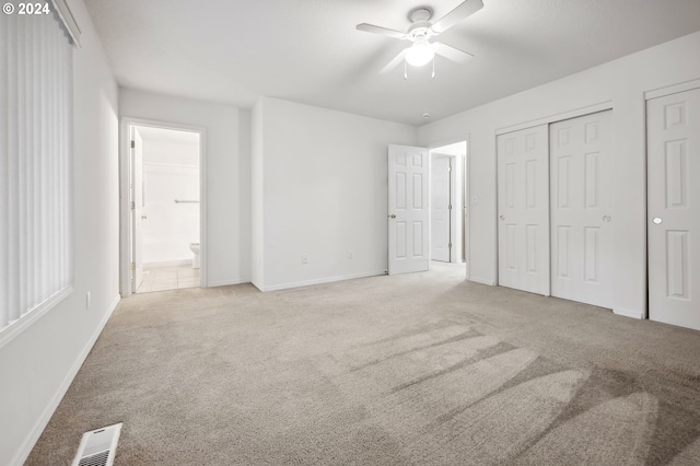 unfurnished bedroom with ensuite bathroom, light carpet, ceiling fan, and two closets