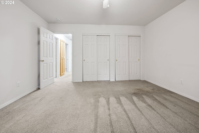 unfurnished bedroom featuring two closets, ceiling fan, and carpet flooring