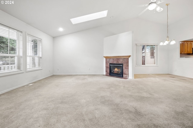 unfurnished living room featuring ceiling fan with notable chandelier, a tiled fireplace, light carpet, and vaulted ceiling