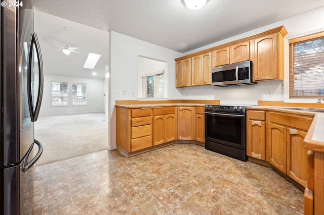 kitchen featuring stainless steel appliances, light colored carpet, a skylight, ceiling fan, and sink