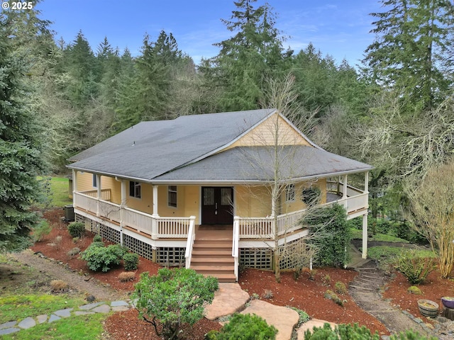 country-style home with covered porch, a shingled roof, stairway, and cooling unit