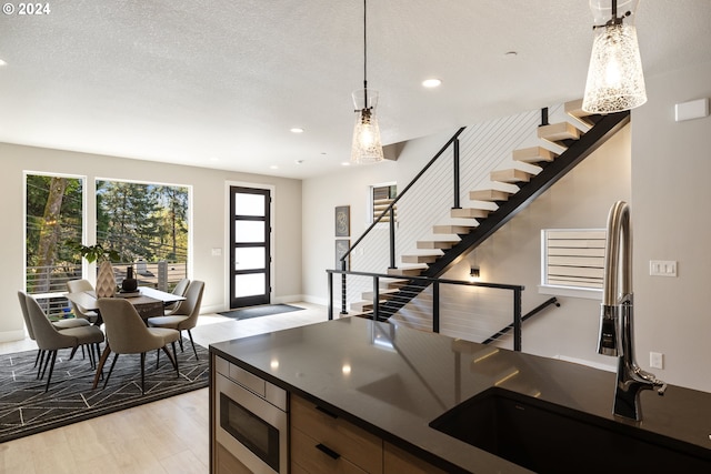 kitchen with a textured ceiling, pendant lighting, light wood-type flooring, and stainless steel microwave