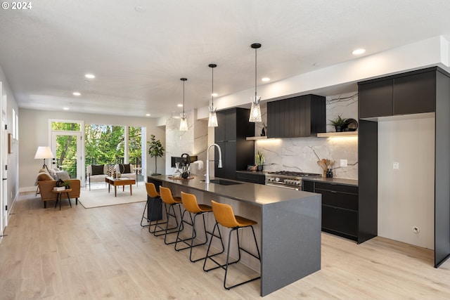 kitchen with decorative light fixtures, a center island with sink, light hardwood / wood-style floors, high end range, and sink