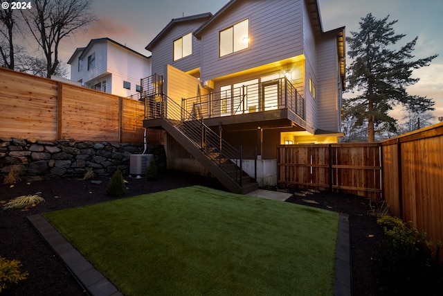 back house at dusk featuring a yard and central air condition unit