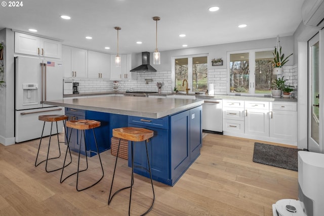 kitchen featuring white cabinets, high end white refrigerator, wall chimney range hood, dishwasher, and a kitchen island