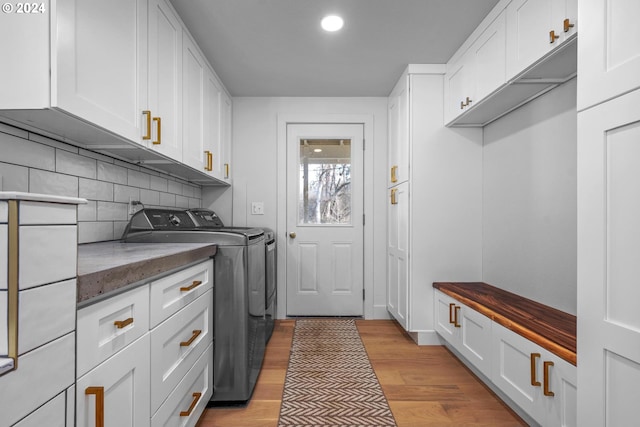 clothes washing area with cabinets, light wood-type flooring, and washer and clothes dryer