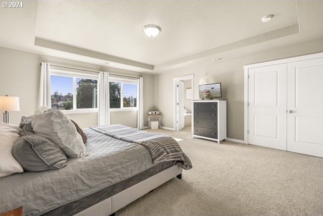 carpeted bedroom with a textured ceiling, ensuite bathroom, and a raised ceiling