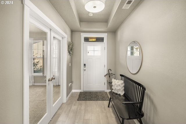 entrance foyer with light hardwood / wood-style floors, plenty of natural light, a raised ceiling, and french doors