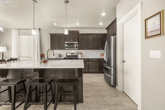 kitchen with pendant lighting, appliances with stainless steel finishes, a kitchen bar, an island with sink, and light hardwood / wood-style flooring