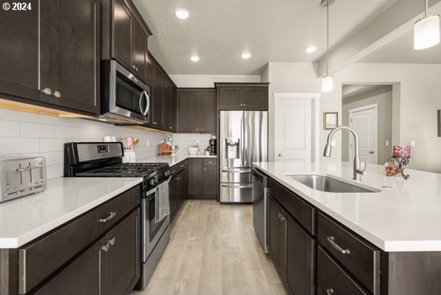 kitchen featuring pendant lighting, sink, light wood-type flooring, appliances with stainless steel finishes, and an island with sink