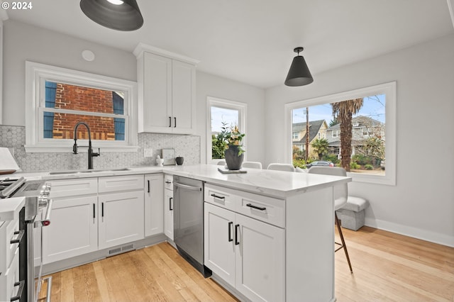 kitchen with appliances with stainless steel finishes, sink, decorative light fixtures, light hardwood / wood-style floors, and white cabinetry