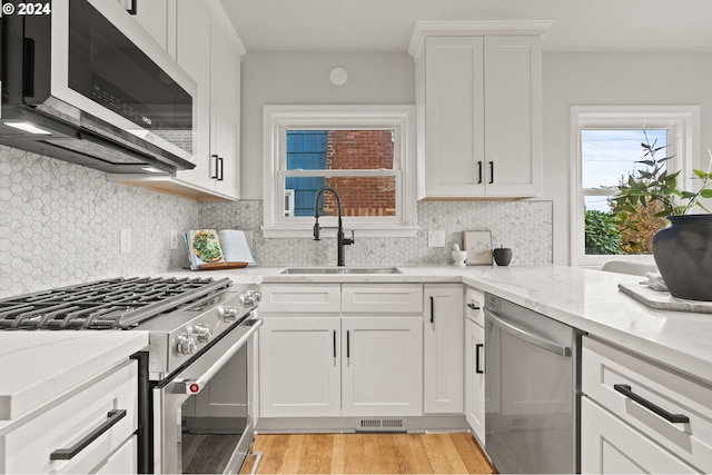 kitchen with sink, appliances with stainless steel finishes, light hardwood / wood-style floors, light stone counters, and white cabinetry