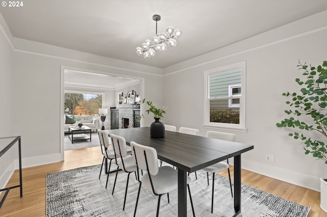 dining area with a brick fireplace, hardwood / wood-style floors, an inviting chandelier, and ornamental molding