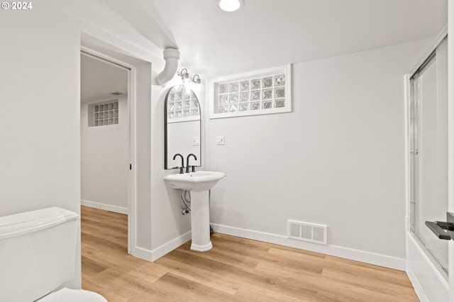 bathroom featuring shower / bath combination with glass door, hardwood / wood-style flooring, and toilet