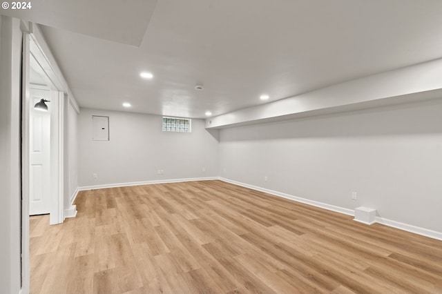 basement featuring electric panel and light hardwood / wood-style flooring