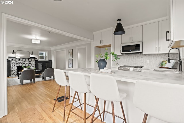 kitchen with a tile fireplace, white cabinetry, light stone countertops, sink, and light hardwood / wood-style floors