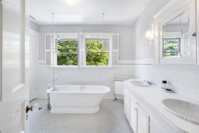 bathroom featuring a sink, a freestanding bath, wainscoting, tile patterned floors, and double vanity