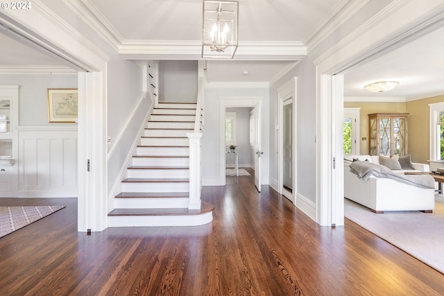 foyer with a decorative wall, stairway, ornamental molding, wood finished floors, and a chandelier