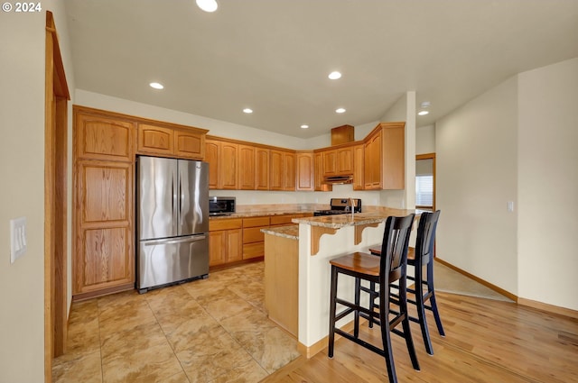 kitchen featuring light stone countertops, a kitchen breakfast bar, stainless steel appliances, and light hardwood / wood-style flooring