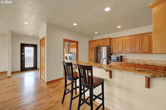 kitchen with light stone countertops, light hardwood / wood-style flooring, a kitchen bar, washer and dryer, and appliances with stainless steel finishes