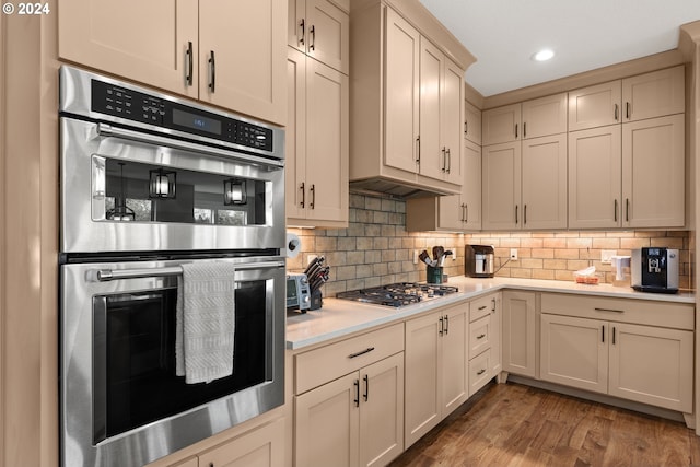 kitchen with hardwood / wood-style flooring, decorative backsplash, appliances with stainless steel finishes, and cream cabinetry