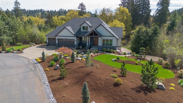 craftsman-style house with a garage, driveway, stone siding, and a view of trees