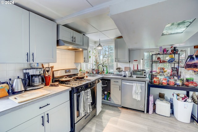 kitchen featuring backsplash, light hardwood / wood-style floors, hanging light fixtures, and appliances with stainless steel finishes