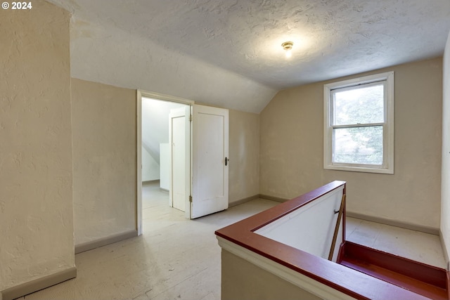 hall featuring lofted ceiling and a textured ceiling