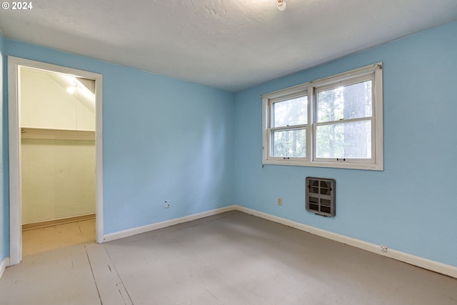 unfurnished bedroom with heating unit, a spacious closet, a closet, and a textured ceiling