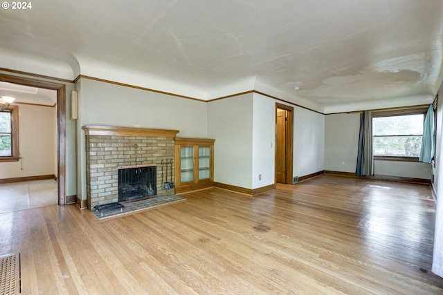 unfurnished living room with ornamental molding, a fireplace, a wealth of natural light, and light hardwood / wood-style flooring