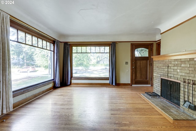 unfurnished living room featuring a wealth of natural light, wood-type flooring, and a brick fireplace