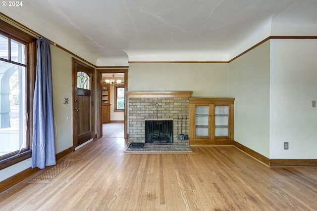 unfurnished living room featuring a brick fireplace, crown molding, an inviting chandelier, and light wood-type flooring