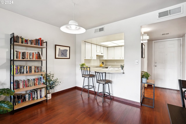 kitchen with white cabinetry, dark wood-type flooring, kitchen peninsula, and a kitchen bar